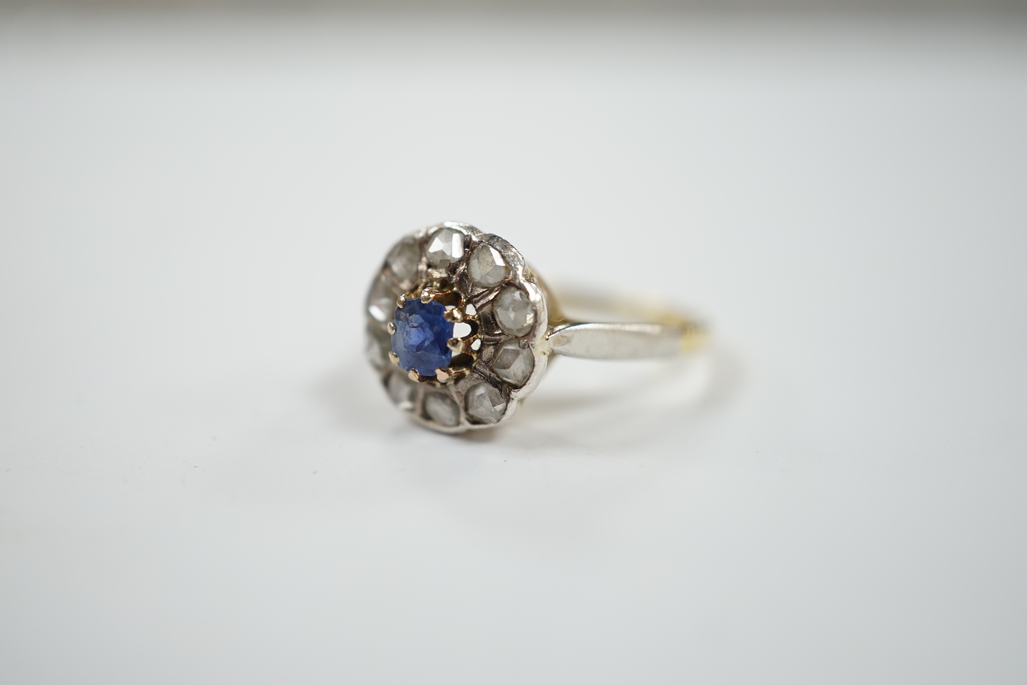 An early 20th century 18ct, single stone sapphire and ten stone rose cut diamond set circular cluster ring, size L, gross weight 3.9 grams.
